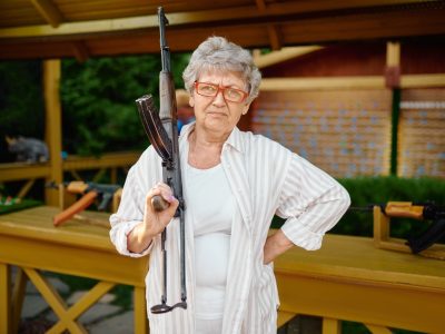 Pretty granny with gun poses in shooting gallery